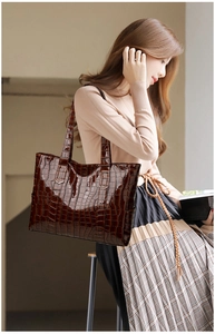 Detail of dark brown tote bag featuring glossy crocodile embossed texture and sturdy handles