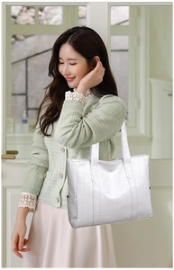 Detailed close-up of white crocodile pattern tote bag held by a model in a minimal room