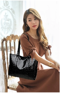 Black crocodile embossed tote bag with high-gloss finish worn on the model's shoulder