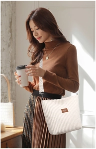 Detail of cream corduroy bucket bag featuring stylish wavy strap and leather patch
