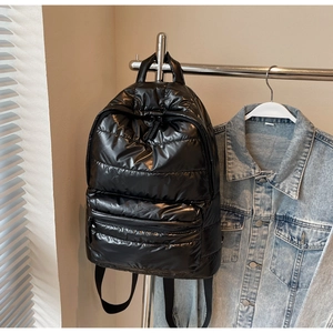 Detail of glossy black quilted puffer backpack showing padded texture and zipper pockets