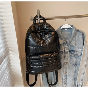 Close-up of black quilted puffer backpack hanging on metal rack with denim jacket