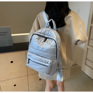 Detail of silver quilted puffer backpack with metallic finish and fabric straps on model