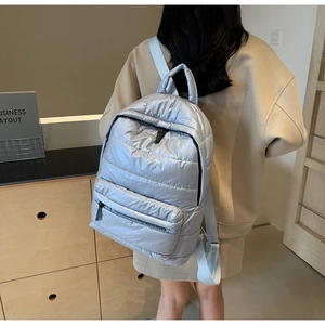Close-up of light blue quilted down backpack on model showing puffer texture and straps