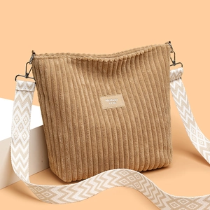 Brown corduroy tote bag with wide patterned shoulder strap on a warm minimal background