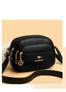 Detail of black pebbled leather crossbody bag with three golden zipper compartments