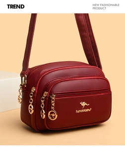 Detail of wine red lychee leather crossbody bag with three golden zipper compartments