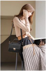 Detail of black crocodile texture handbag with golden square lock and leather top handle