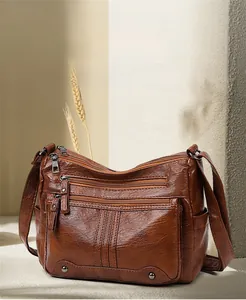 Detail view of brown soft leather crossbody bag with multiple zipper pockets on beige background