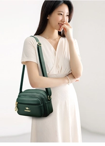 Detail of dark green crossbody bag with three zipper compartments and gold hardware