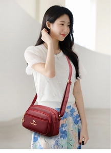 Detail of dark red lychee texture leather crossbody bag with three zipper pockets