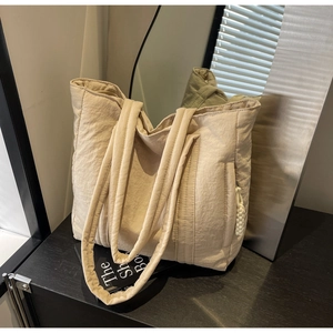 Detail of beige quilted canvas tote bag with textured surface and woven rope accent