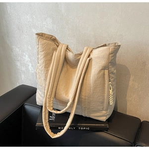 Macro detail of cream quilted nylon tote bag with decorative knotted rope zipper puller