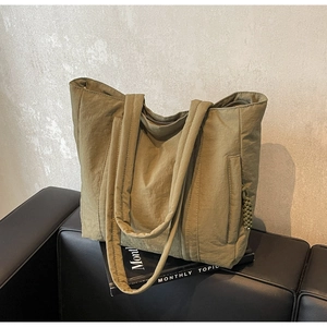 Detail of army green canvas tote bag with side braided charm on a leather sofa