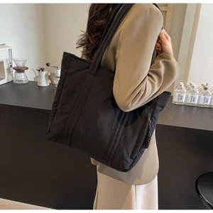Close-up of black quilted canvas tote bag with side zipper detail in coffee shop setting