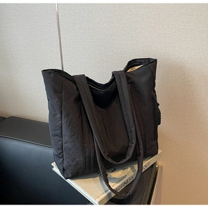 Detail of black nylon tote bag with top zipper closure and dual straps on a leather seat