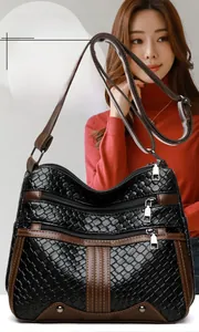 Detail of black woven leather crossbody bag with brown trim and multi-zipper compartments
