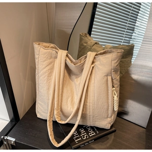 Detail view of beige quilted tote bag with side braided rope charm and smooth zipper