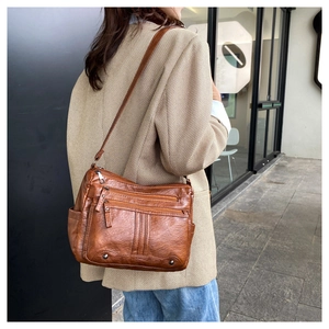 Brown soft leather crossbody bag with multiple pockets worn over a neutral blazer