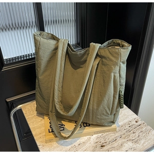 Detail of olive green nylon tote bag featuring side zipper pocket and quilted shoulder strap