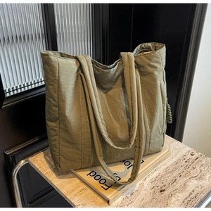 Detail of an olive green nylon tote bag with long handles and a soft quilted texture