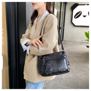 Detail view of a large black soft leather crossbody bag with multiple zippers worn by a model