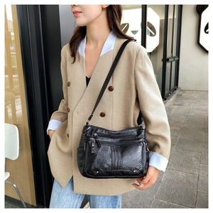 Detail of black multi-pocket crossbody bag showing soft leather texture and zip pockets