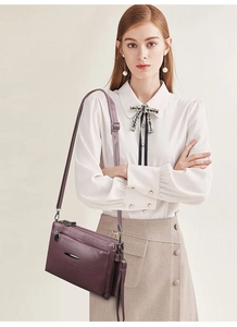 Detail view of purple soft leather crossbody bag with multiple zip pockets on model