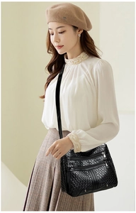 Detail of black faux leather crossbody bag with quilted texture and multi-zipper layers