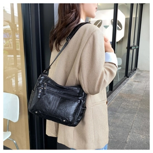 Detail of black pebbled leather crossbody bag with multiple zippers shown on a model