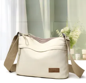 Detail view of cream nylon crossbody bag featuring a brown leather SOSIDI logo label