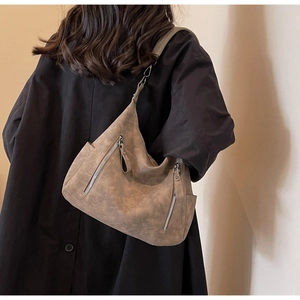 Brown vintage hobo shoulder bag with zipper details worn by a model in a dark coat