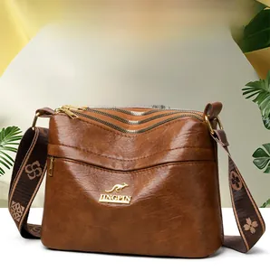 Detail of a brown leather crossbody bag featuring three zipper layers and wide woven strap