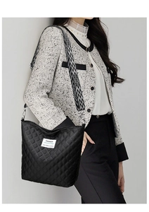 Detail of black quilted shoulder bag with patterned strap shown on a model