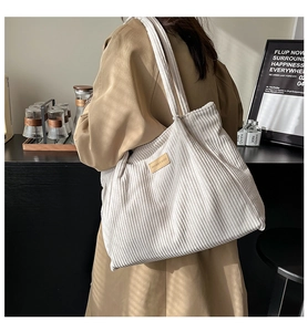 Detail of off-white corduroy tote bag texture and leather patch in a cafe setting