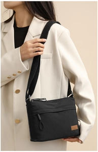 Detailed side view of black lightweight nylon crossbody bag styled with a white blazer