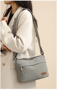 Grey nylon crossbody bag with multi-layer zipper pockets worn with a beige blazer