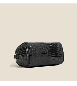Détail du sac cylindrique noir avec motif crocodile, finition vernie et anneau doré élégant