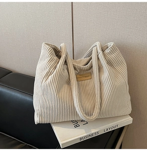 Détail de la texture d'un sac cabas en velours côtelé beige avec logo en cuir sur un livre