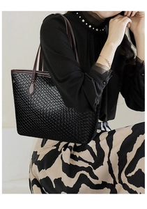 Detail of black tote bag with woven texture and long brown straps worn by model
