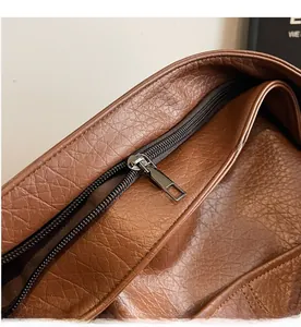 Detailansicht des Metallreißverschlusses und der Narbenlederstruktur dieser braunen Tasche