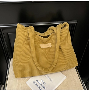 Gros plan d'un sac cabas en velours côtelé jaune moutarde avec texture et logo en cuir