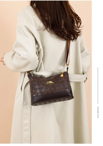 Dettaglio borsa a tracolla marrone scuro con trama intrecciata e logo dorato su trench beige