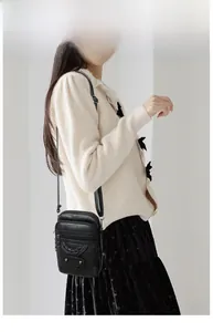 Model wearing a black soft leather crossbody phone bag with woven details and metal studs