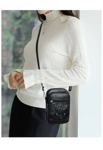 Detail of a black leather mini crossbody bag with woven accents and silver hardware