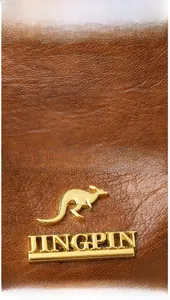 Detail of brown litchi grain leather texture and gold kangaroo metal logo on crossbody bag