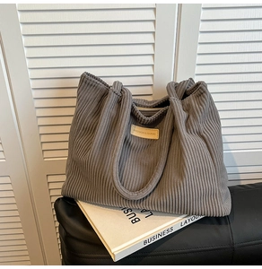 Détail d'un cabas en velours côtelé gris foncé avec écusson en cuir et texture douce unique