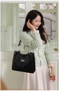 Close-up detail of black corduroy tote bag with metallic chain strap and logo
