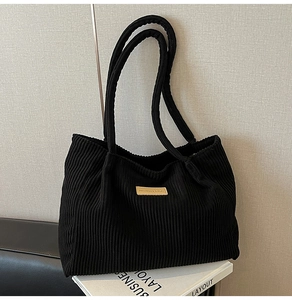 Detail of black corduroy tote bag featuring a leather logo patch and vertical texture