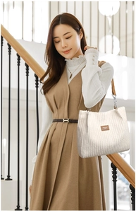 Detail of white corduroy tote bag featuring leather patch and metal chain strap